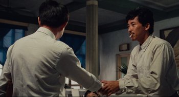 Movie still from “Boat People” (1982), directed by Ann Hui – Two men are shaking hands in a room; Medium shot, Over the shoulder angle