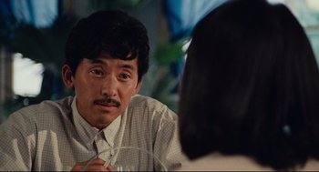 Movie still from “Boat People” (1982), directed by Ann Hui – A man sitting at a table with a glass of wine; Close Up shot, Over the shoulder angle