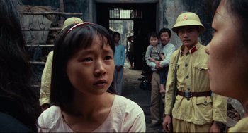 Movie still from “Boat People” (1982), directed by Ann Hui – A group of people standing around a building; Close Up shot, Over the shoulder angle