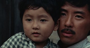 Movie still from “Boat People” (1982), directed by Ann Hui – A man and a boy are looking at the camera; Close Up shot, High angle
