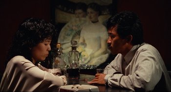 Movie still from “Boat People” (1982), directed by Ann Hui – Two people sitting at a table with a glass of wine; Medium shot, Over the shoulder angle