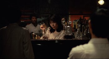 Movie still from “Boat People” (1982), directed by Ann Hui – A woman sitting at a bar smoking a cigarette; Medium shot, Over the shoulder angle