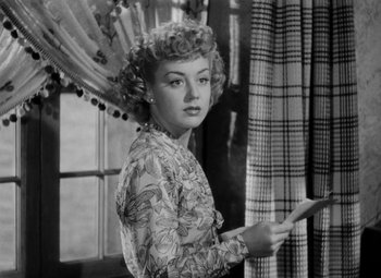 Movie still from “Bombardier” (1943), directed by Lambert Hillyer – A black - and - white photo of a woman in a floral dress; Close Up shot, Low angle