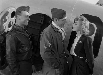 Movie still from “Bombardier” (1943), directed by Lambert Hillyer – A couple of men and a woman standing next to each other; Medium shot, Over the shoulder angle
