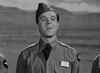 Movie still from “Bombardier” (1943), directed by Lambert Hillyer – A man in a military uniform standing in front of mountains; Close Up shot, Low angle