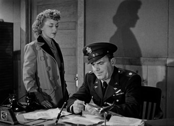 Movie still from “Bombardier” (1943), directed by Lambert Hillyer – An old photo of a man and a woman at a table; Medium shot, Low angle