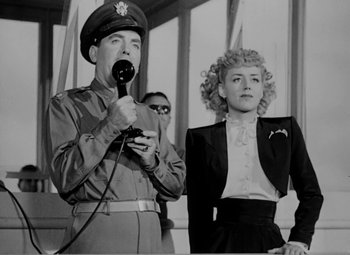 Movie still from “Bombardier” (1943), directed by Lambert Hillyer – A man and a woman are standing next to each other; Medium shot, Low angle