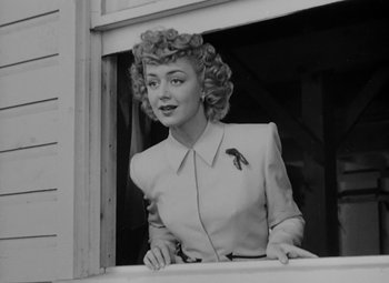 Movie still from “Bombardier” (1943), directed by Lambert Hillyer – An old black and white photo of a woman looking out of a window; Medium shot, Low angle
