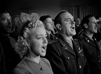 Movie still from “Bombardier” (1943), directed by Lambert Hillyer – A group of men and women singing in a room; Medium shot, Low angle