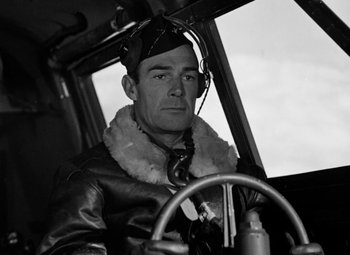 Movie still from “Bombardier” (1943), directed by Lambert Hillyer – A man in a pilot's uniform sitting in the cockpit of an airplane; Medium shot, High angle