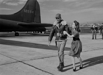 Movie still from “Bombardier” (1943), directed by Lambert Hillyer – A man and a woman walking towards an airplane on a runway; Wide shot, Low angle