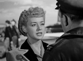 Movie still from “Bombardier” (1943), directed by Lambert Hillyer – An old black and white photo of a woman talking to a man; Medium shot, Over the shoulder angle