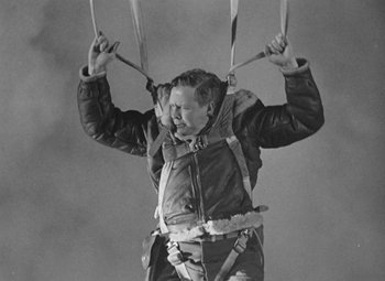 Movie still from “Bombardier” (1943), directed by Lambert Hillyer – A man in a parka hanging from a parachute; Medium shot, Low angle