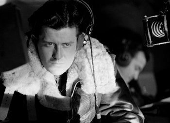 Movie still from “Bombardier” (1943), directed by Lambert Hillyer – A man with a fur collar is listening to music with headphones; Close Up shot, Low angle