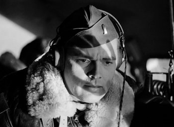 Movie still from “Bombardier” (1943), directed by Lambert Hillyer – A man in a pilot's uniform with headphones on; Close Up shot, Low angle