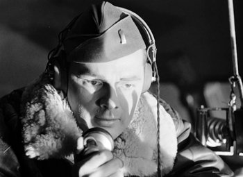 Movie still from “Bombardier” (1943), directed by Lambert Hillyer – A man wearing a hat and holding a camera; Close Up shot, Low angle