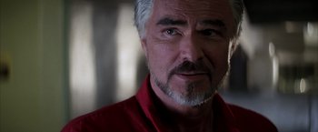 Movie still from “Boogie Nights” (1997), directed by Paul Thomas Anderson – An older man wearing a red shirt looking at the camera; Close Up shot, Over the shoulder angle