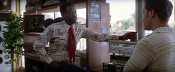 Movie still from “Boogie Nights” (1997), directed by Paul Thomas Anderson – A man wearing a red neck tie and a floral shirt; Medium shot, Low angle