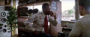 Movie still from “Boogie Nights” (1997), directed by Paul Thomas Anderson – A man wearing a tie drinking from a mug; Medium shot, Low angle