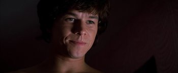 Movie still from “Boogie Nights” (1997), directed by Paul Thomas Anderson – A young man is smiling for the camera in the dark; Close Up shot, Low angle