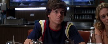 Movie still from “Boogie Nights” (1997), directed by Paul Thomas Anderson – A man sitting at a table with a glass of wine; Close Up shot, Over the shoulder angle