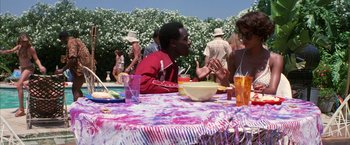Movie still from “Boogie Nights” (1997), directed by Paul Thomas Anderson – A man sitting at a table in front of a group of people; Medium shot, High angle