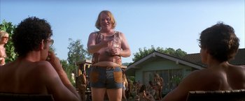 Movie still from “Boogie Nights” (1997), directed by Paul Thomas Anderson – A man in shorts and a tank top standing in front of a group of people; Medium shot, Low angle