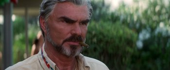 Movie still from “Boogie Nights” (1997), directed by Paul Thomas Anderson – An older man smoking a cigarette in front of trees; Close Up shot, Low angle