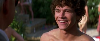 Movie still from “Boogie Nights” (1997), directed by Paul Thomas Anderson – A young man smiles while standing next to a swimming pool; Close Up shot, Low angle