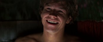 Movie still from “Boogie Nights” (1997), directed by Paul Thomas Anderson – A young man smiling for the camera with no shirt on; Close Up shot, Low angle