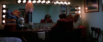 Movie still from “Boogie Nights” (1997), directed by Paul Thomas Anderson – A man sitting at a table in front of a mirror; Wide shot, High angle