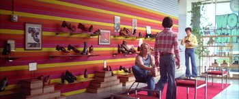 Movie still from “Boogie Nights” (1997), directed by Paul Thomas Anderson – Two people standing in front of a wall with shoes on it; Wide shot, Low angle