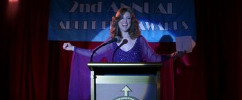 Movie still from “Boogie Nights” (1997), directed by Paul Thomas Anderson – A woman standing at a podium in front of a microphone; Medium shot, Low angle