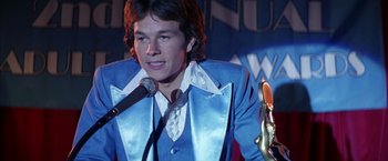 Movie still from “Boogie Nights” (1997), directed by Paul Thomas Anderson – A man in a blue suit holding a microphone; Close Up shot, Low angle