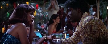 Movie still from “Boogie Nights” (1997), directed by Paul Thomas Anderson – A man and a woman are sitting at a table; Medium shot, Low angle