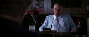Movie still from “Boogie Nights” (1997), directed by Paul Thomas Anderson – A man sitting at a table in front of another man in a suit; Medium shot, Low angle