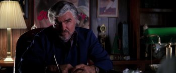Movie still from “Boogie Nights” (1997), directed by Paul Thomas Anderson – An older man sitting at a table in front of a painting; Close Up shot, Low angle