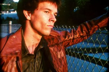Movie still from “Boogie Nights” (1997), directed by Paul Thomas Anderson – A man in a leather jacket leaning against a fence; Close Up shot, Low angle