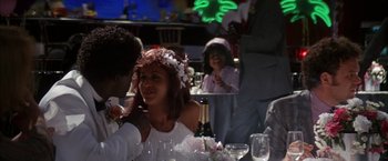 Movie still from “Boogie Nights” (1997), directed by Paul Thomas Anderson – Two people sitting at a table with a bottle of champagne; Medium shot, Over the shoulder angle