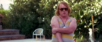 Movie still from “Boogie Nights” (1997), directed by Paul Thomas Anderson – A man in a striped shirt is sitting on the ground; Medium shot, Low angle