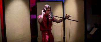 Movie still from “Boogie Nights” (1997), directed by Paul Thomas Anderson – A man in a red shirt is singing into a microphone; Medium shot, Low angle