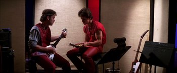 Movie still from “Boogie Nights” (1997), directed by Paul Thomas Anderson – A man sitting on top of a chair holding a guitar; Medium shot, Low angle