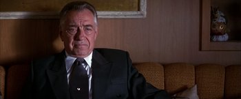 Movie still from “Boogie Nights” (1997), directed by Paul Thomas Anderson – An older man wearing a suit and tie sitting on a couch; Close Up shot, Low angle