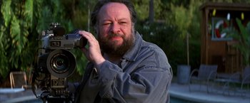 Movie still from “Boogie Nights” (1997), directed by Paul Thomas Anderson – A man with a beard is taking a picture with a camera; Close Up shot, Low angle