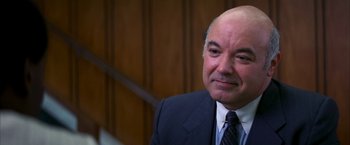 Movie still from “Boogie Nights” (1997), directed by Paul Thomas Anderson – A man in a suit and tie in front of a wooden wall; Close Up shot, Over the shoulder angle