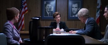 Movie still from “Boogie Nights” (1997), directed by Paul Thomas Anderson – A woman sitting at a table in front of a wall with pictures on it; Medium shot, Over the shoulder angle