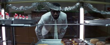 Movie still from “Boogie Nights” (1997), directed by Paul Thomas Anderson – A man standing in front of a display of doughnuts; Medium shot, High angle