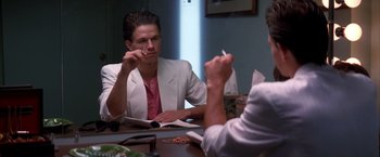 Movie still from “Boogie Nights” (1997), directed by Paul Thomas Anderson – A man sitting at a table in front of another man holding a cigarette; Medium shot, Over the shoulder angle