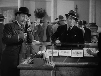 Movie still from “Boom Town” (1940), directed by Jack Conway – Two men in suits and hats are talking on a phone; Medium shot, High angle
