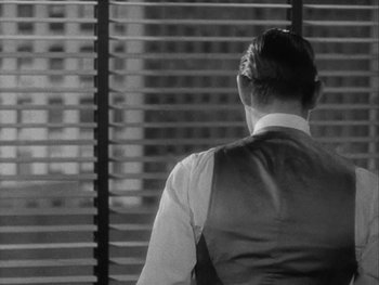 Movie still from “Boom Town” (1940), directed by Jack Conway – A man in a vest looking out of a window; Medium shot, Over the shoulder angle